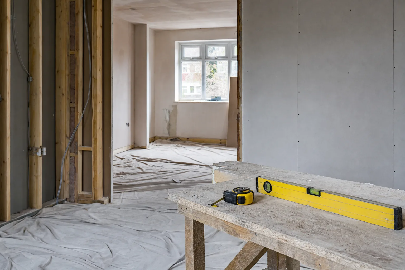 Room mid-renovation with fresh plasterboard, dust sheets and a spirit level resting on a timber workbench